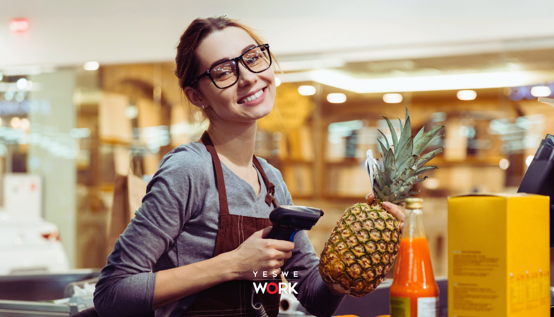 Giovane donna sorridente intenta ad etichettare un'ananas mentre lavora in un supermercato