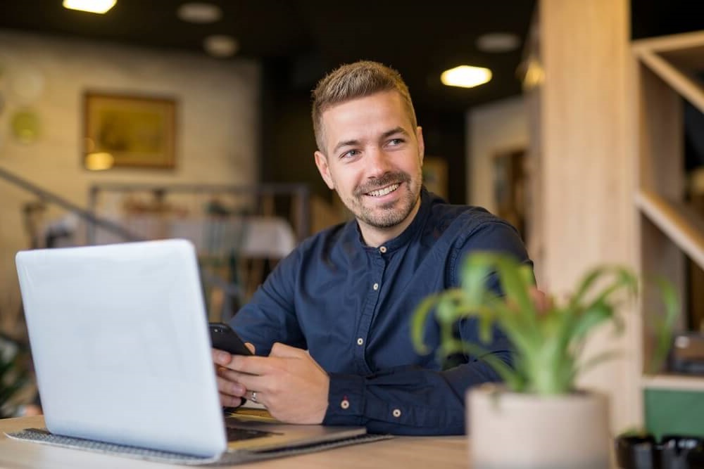 Uomo seduto a una scrivania con laptop e telefono sorride per i Benefit offerti da YesWeWork