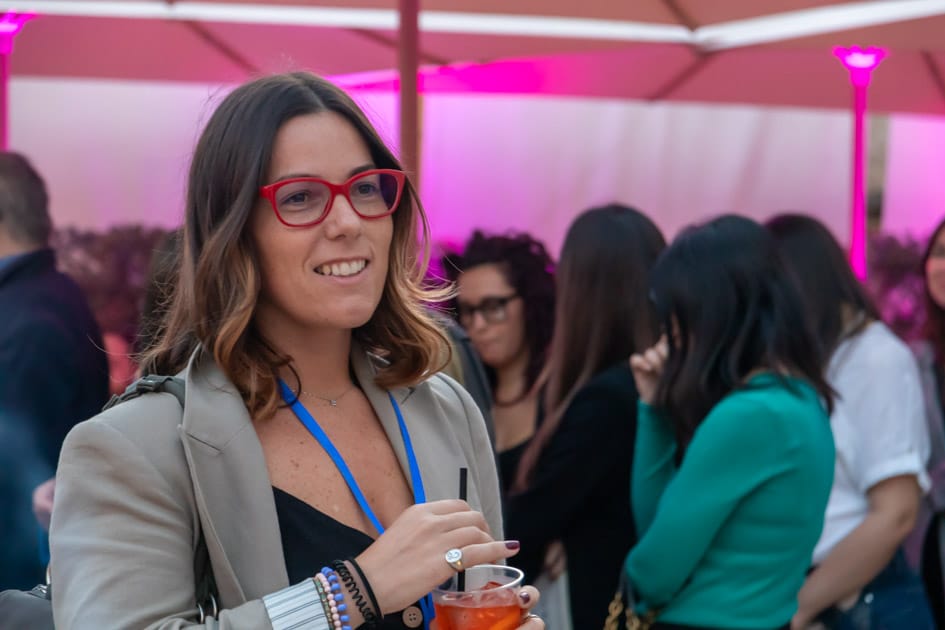 Una partecipante ospite di YesWeWork all'ApeRecruiting Job Day Trani sorseggia il suo spritz e sorride guardandosi attorno