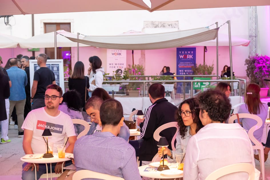 Gente che si rilassa godendosi un aperitivo ai tavoli durante l'ApeRecruiting Job Day di trani in un'atmosfera serena
