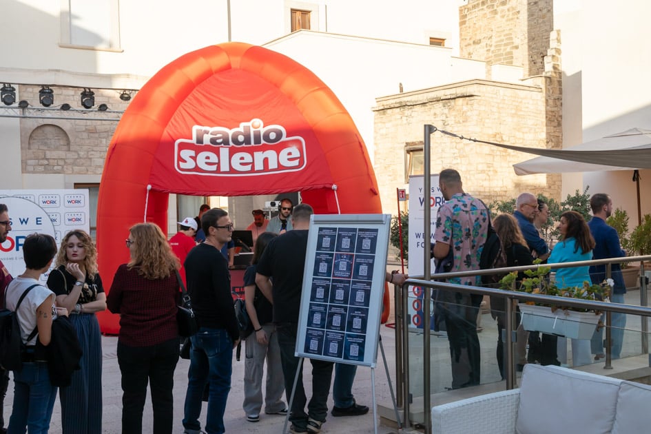 Vista frontale del box di Radio Selene. Di fronte, la fila di candidati in attesa di colloquio all'ApeRecruiting Trani