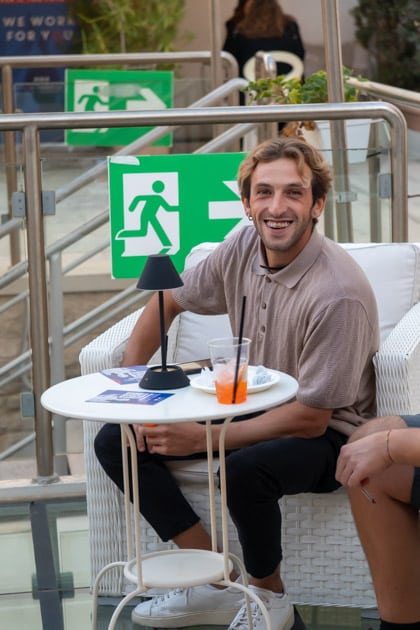 Un ragazzo sorridente, dall'aria molto soddisfatta, sta seduto ad un tavolino a bere uno spritz durante l'ApeRecruiting