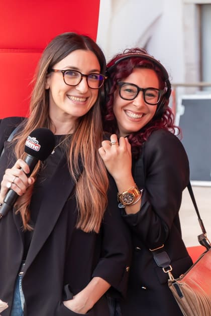 Due ragazze posano sorridenti per una foto con il microfono di radio selene in mano durante l'ApeRecruiting Job Day Trani