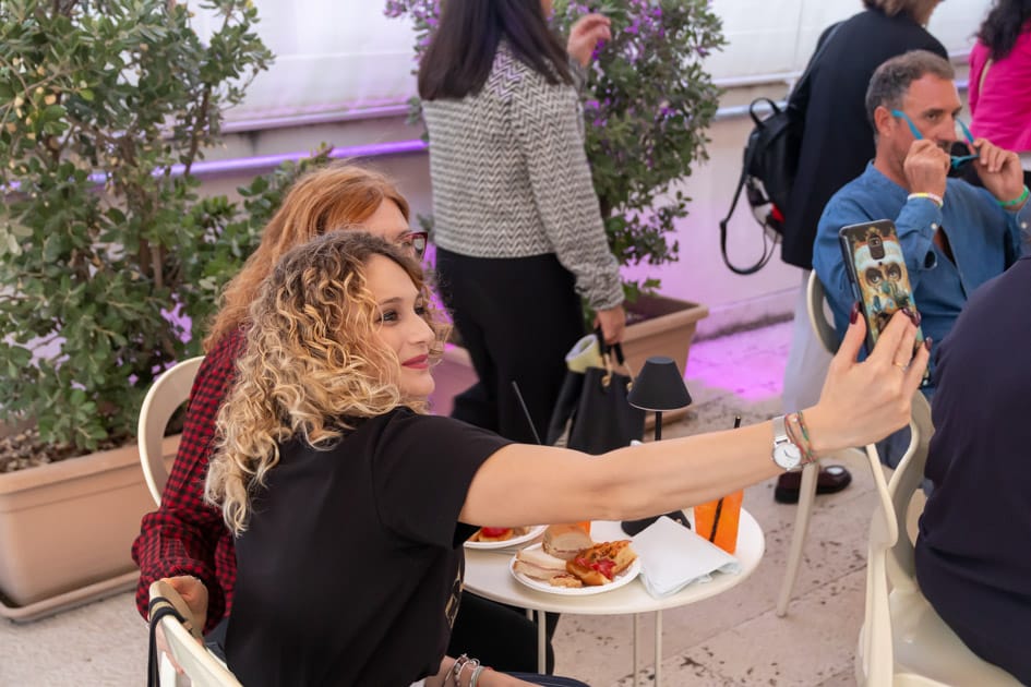 Due ragazze si fanno un selfie mentre sono sedute ad un tavolino dell'area aperitivo all'ApeRecruiting Job Day di Trani