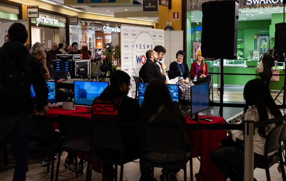Foto laterale del palco di YesWeNERD. In primo piano l'area gaming Nintendo, sullo sfondo Luca Catalano intervista i tre ospiti