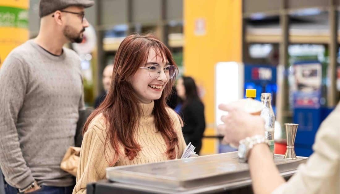 Una giovane ragazza sorride allegramente mentre le viene passato un drink dal barista dell'ApeRecruiting Casamassima