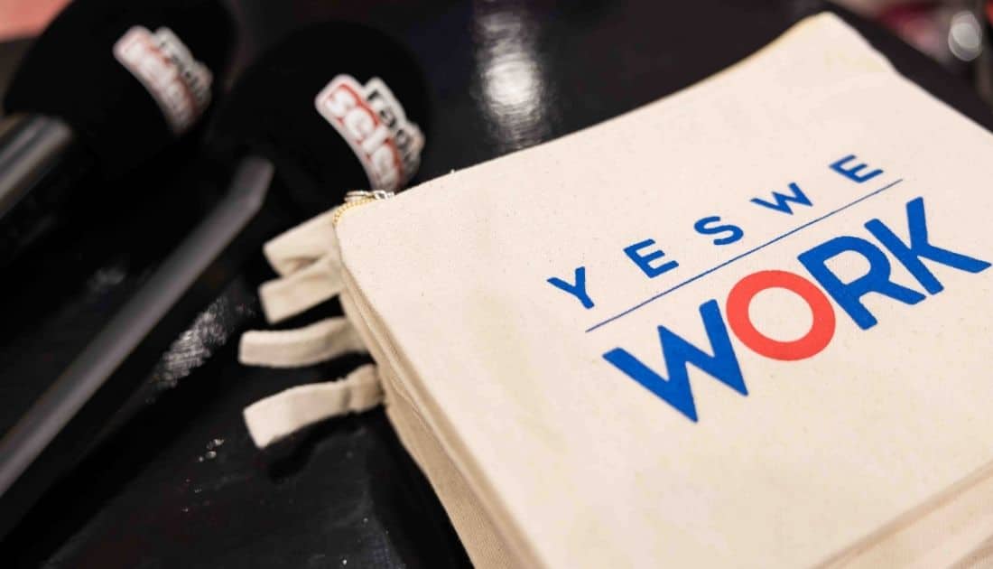 Su un ripiano nero sono poggiate alcune pochette omaggio brandizzate 'YesWeWork' e due microfoni con il logo di Radio Selene