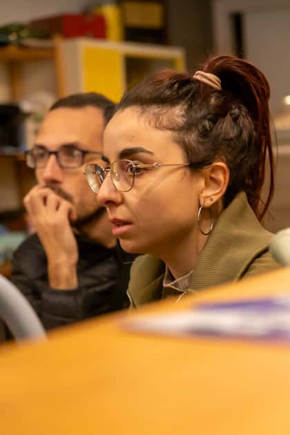 Primo piano sui volti di un ragazzo e una ragazza che seguono attentamente la relatrice durante 'Caffè con YesWeWork'