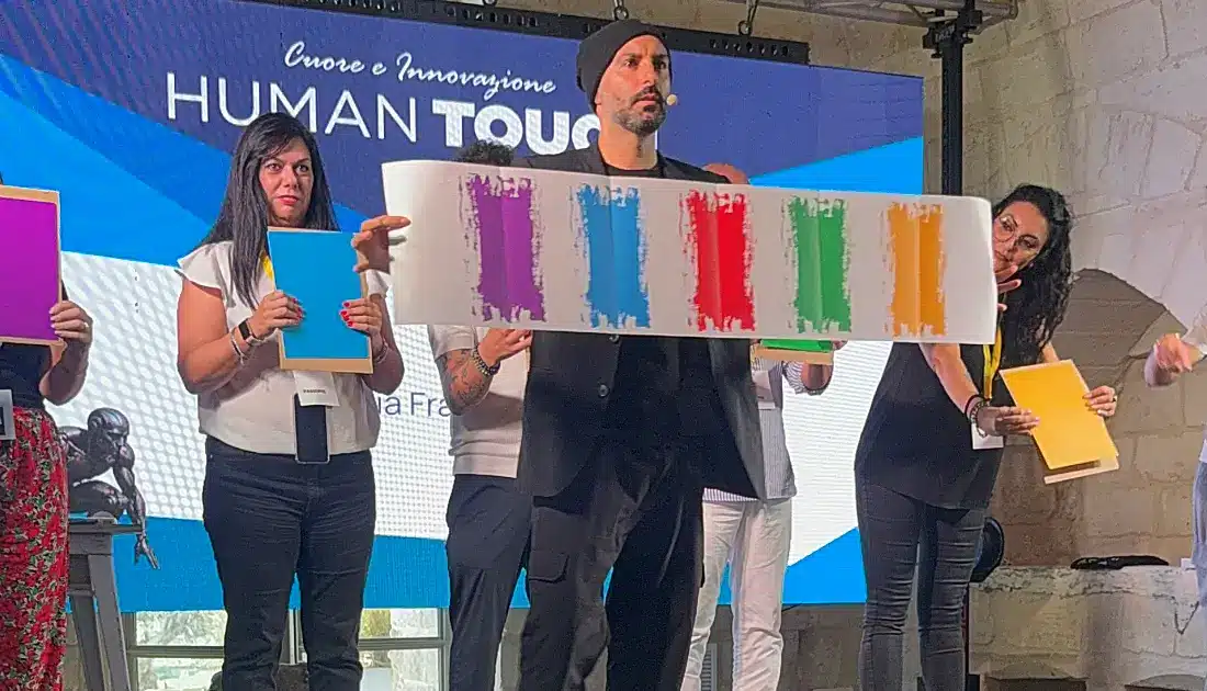Andrea Paris mostra una striscia di carta con una serie di colori uguali a quelli in mano alle persone alle sue spalle
