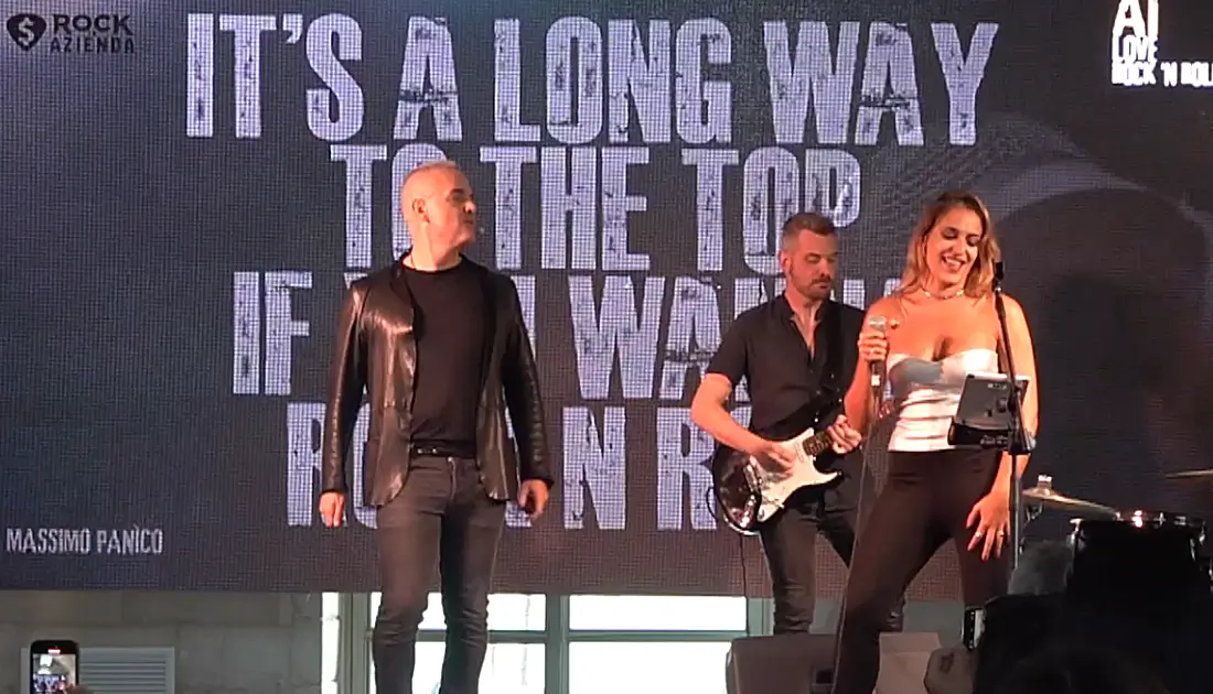 Max Panìco e band sul palco. Sul maxischermo compare la scritta 'It's a long Way To the top if you wanna rock n roll'